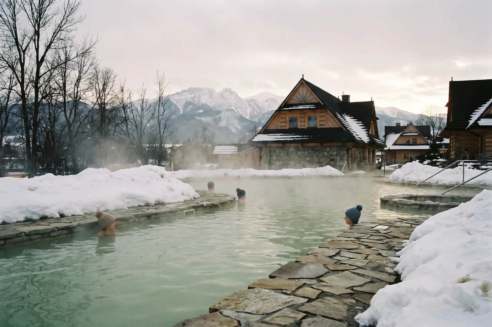 Drewniane baseny geotermalne Gorący Potok w Szaflarach - para nad mleczno-siarkową wodą termalną, w tle zaśnieżone Tatry i las sosnowy