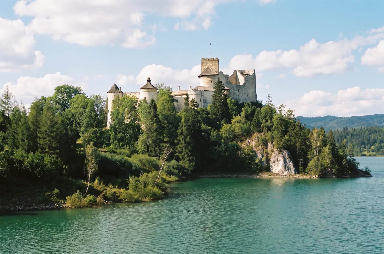 Średniowieczny zamek Dunajec w Niedzicy na wapiennej skale nad turkusowym Jeziorem Czorsztyńskim, z lesistymi szczytami Pienin w tle
