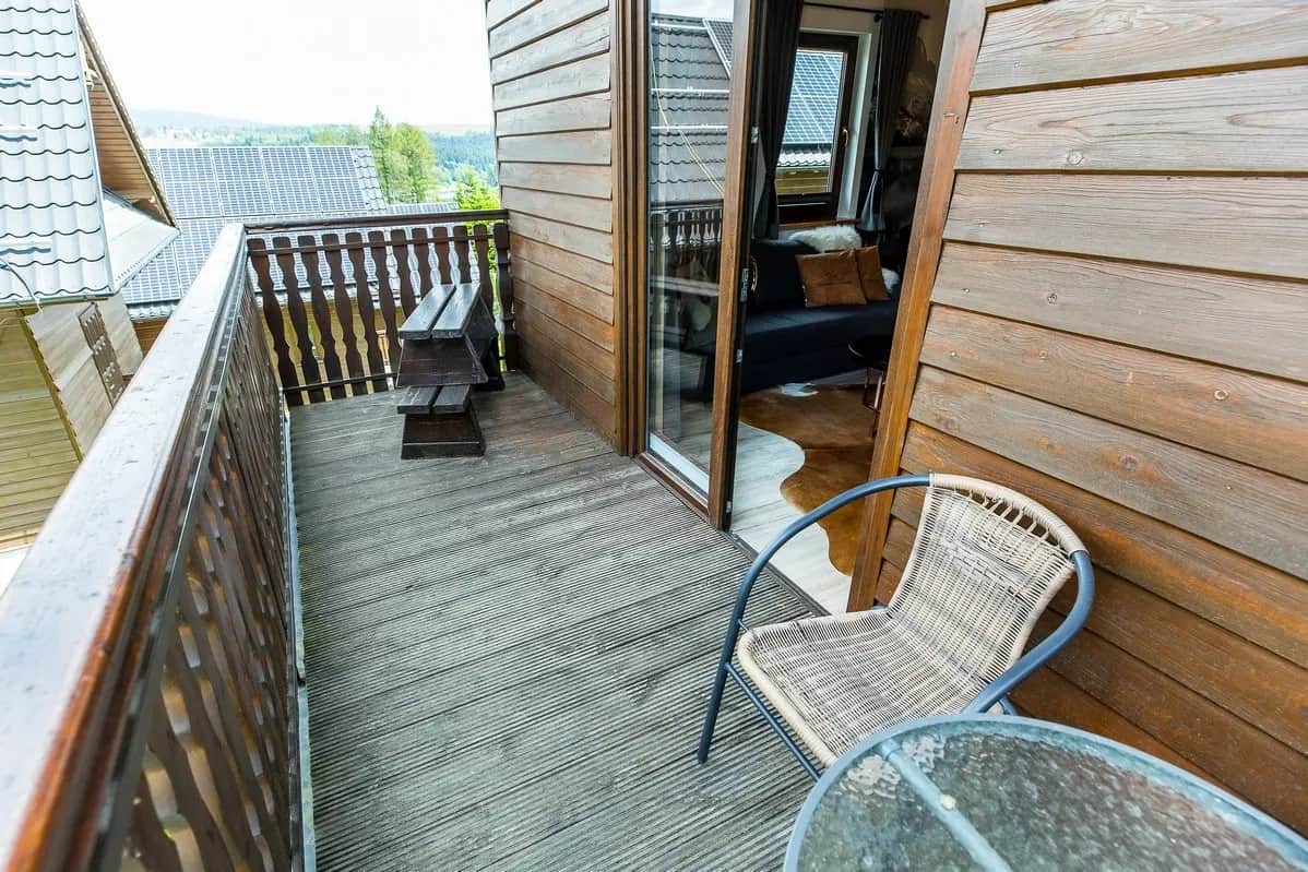 Drewniany balkon z wiklinowym fotelem, szklanym stolikiem i ławką, z widokiem na okolicę