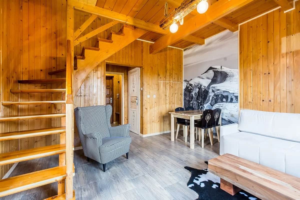 Salon z fotelem, kącikiem jadalnym i fototapetą górską przy drewnianych schodach