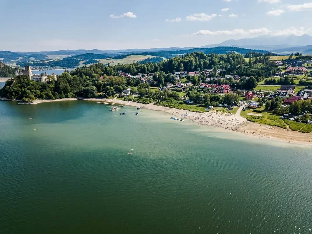 Plaża nad jeziorem z zamkiem na cyplu i górami w tle