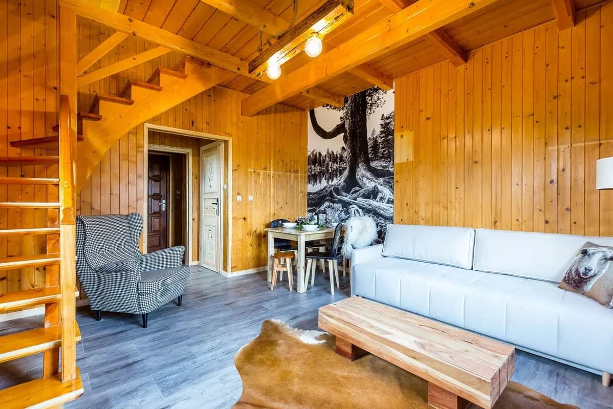 Salon z jasną sofą, drewnianym stolikiem, fotelem i skórą na podłodze pod skosem dachu