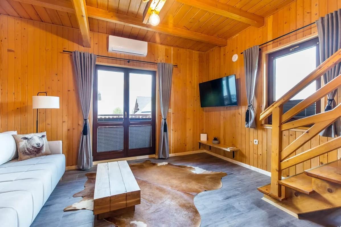 Przestronny salon z białą sofą, telewizorem, schodami na poddasze i drzwiami balkonowymi