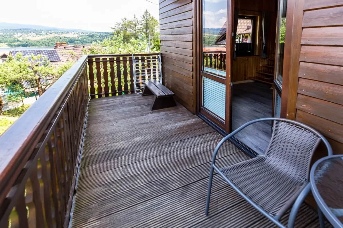 Drewniany balkon z krzesłem i ławką oraz widokiem na zieleń i okoliczne wzgórza
