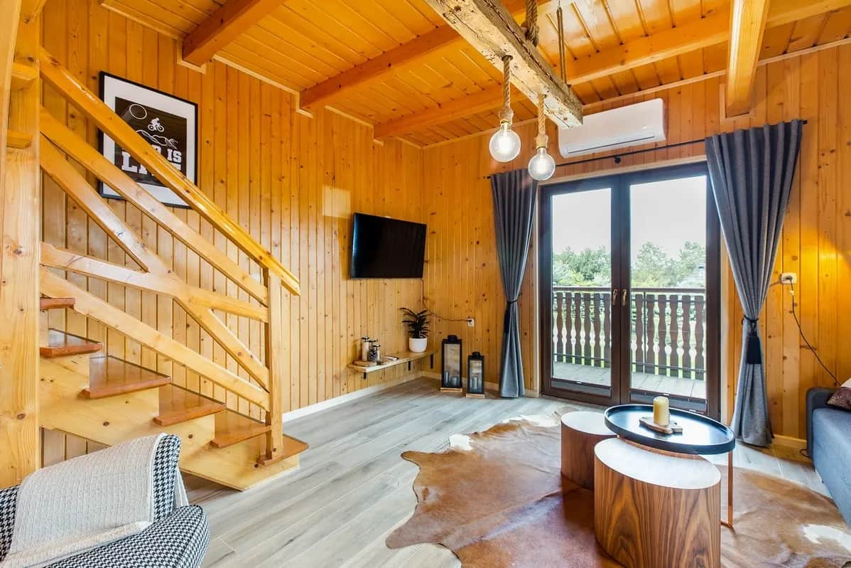 Salon z TV na ścianie, schodami i wyjściem na balkon