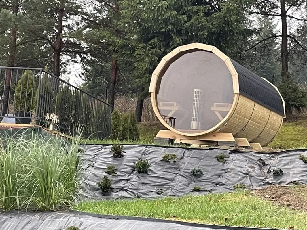 Drewniana sauna beczkowa na ogrodzonym tarasie wśród sosen